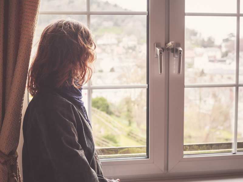 A woman looking out of a window. In-house estimates may incur fees 