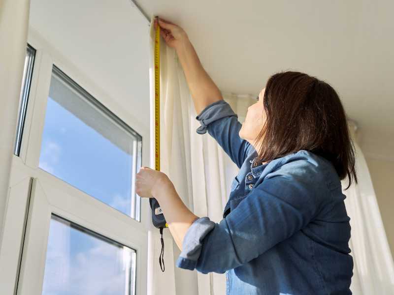 A tape measure extends from bottom to top of window frame. Width and height measurements are noted on a notepad